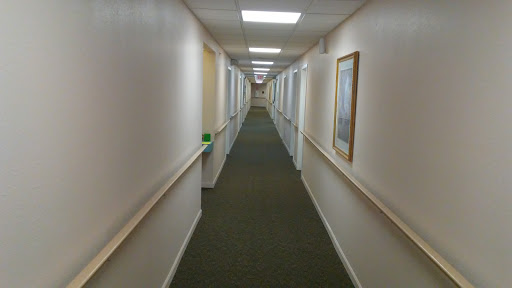 A long, well-lit hallway with green carpet and framed pictures on the walls.