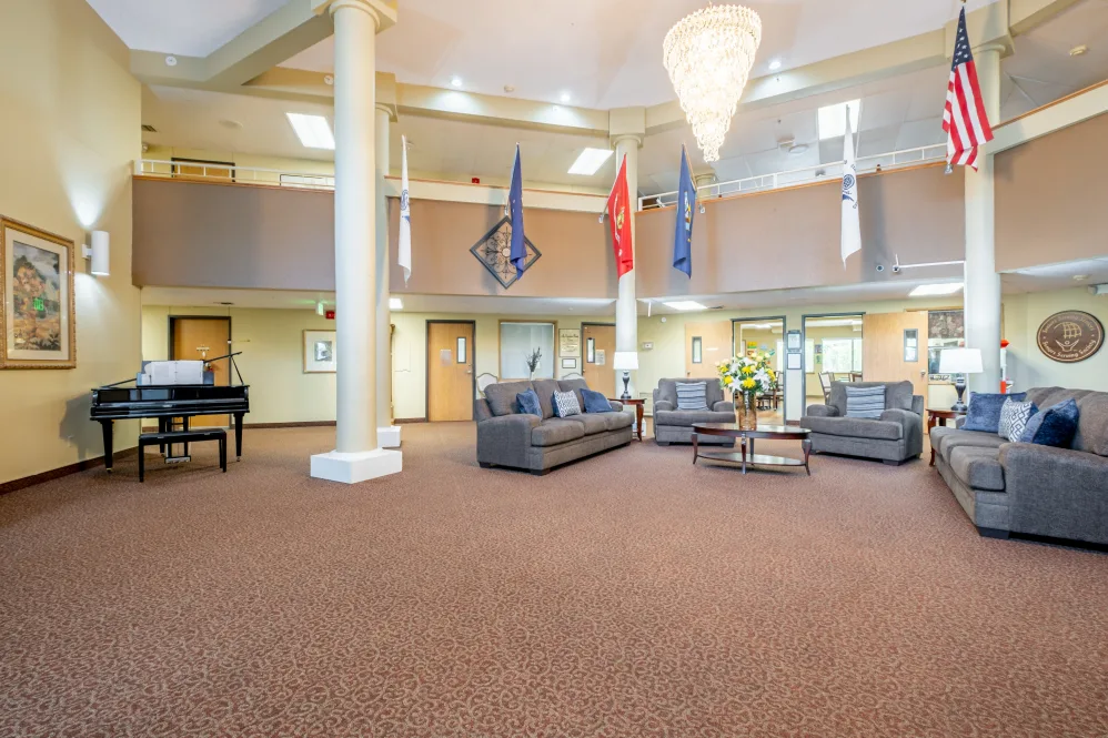 A spacious lobby area with sofas and flags displayed, featuring a large chandelier and carpeted flooring.