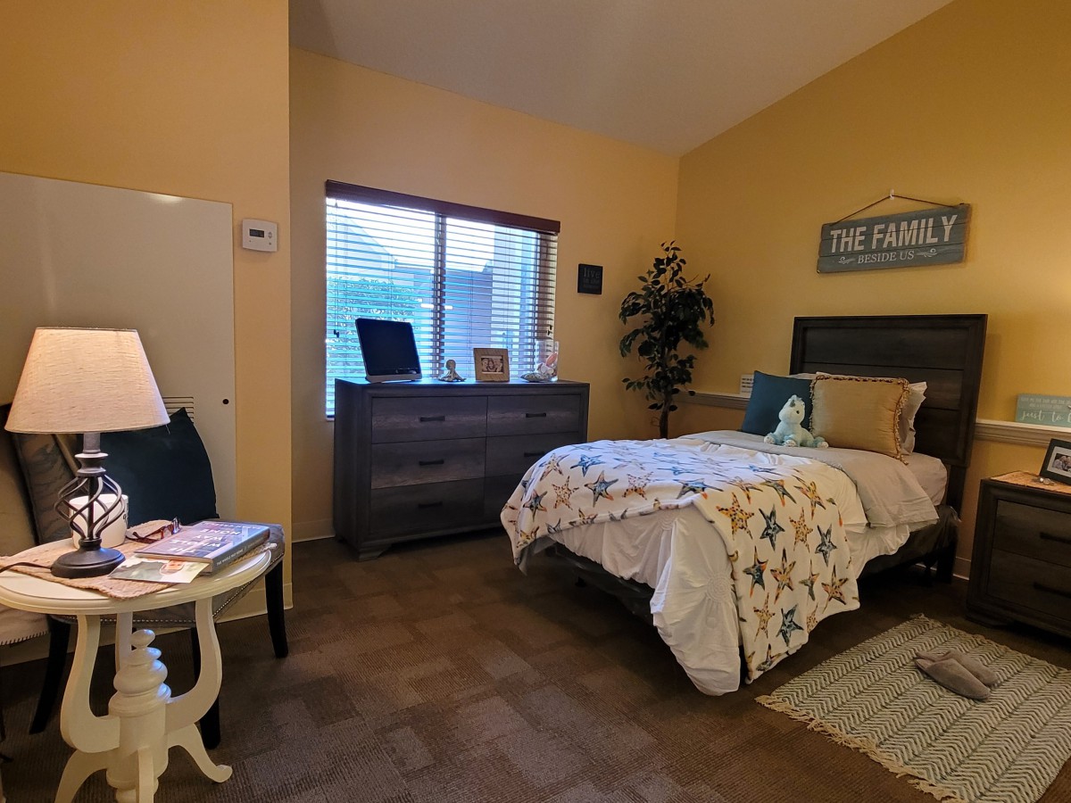 A cozy bedroom with a neatly made bed, decorated in warm tones and featuring a dresser by the window.