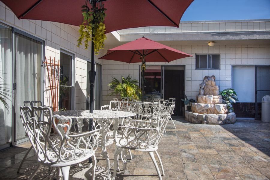 A sunny patio with wrought iron tables and chairs under red umbrellas.