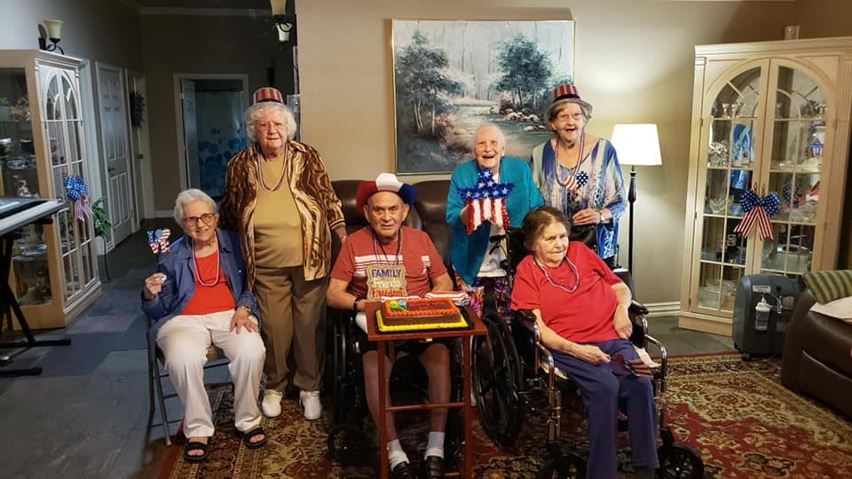 A group of elderly individuals celebrating with a cake and wearing party hats indoors.
