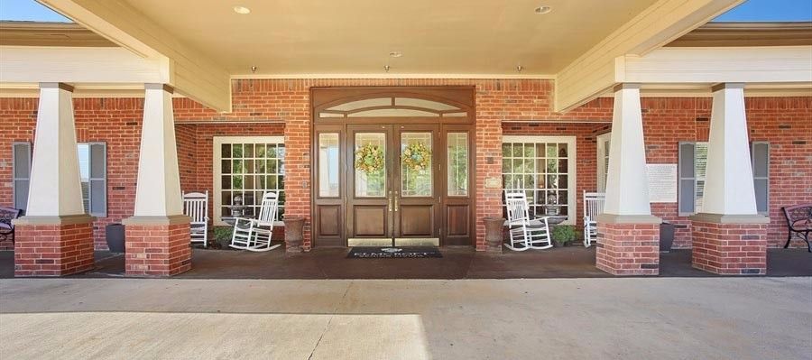 Entrance of a brick building with large wooden doors and rocking chairs on the porch.