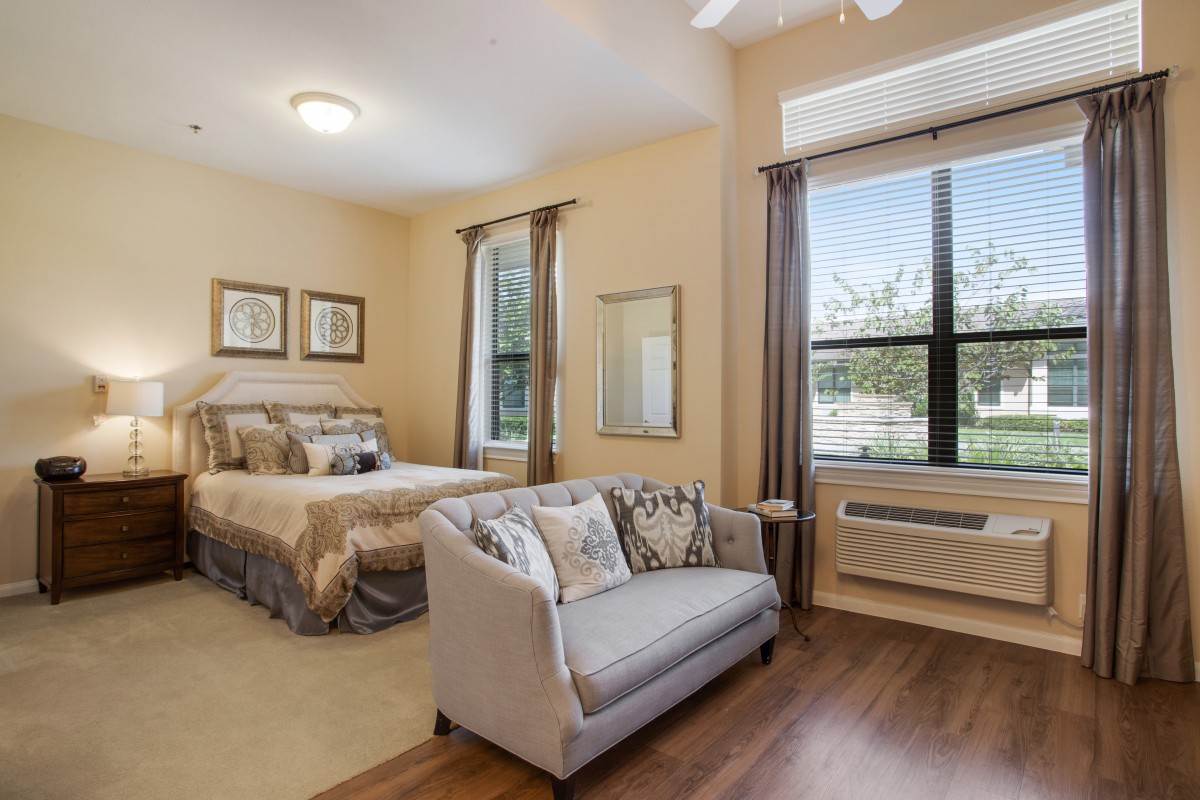A cozy bedroom with a double bed and a small couch, featuring warm tones and bright natural lighting.