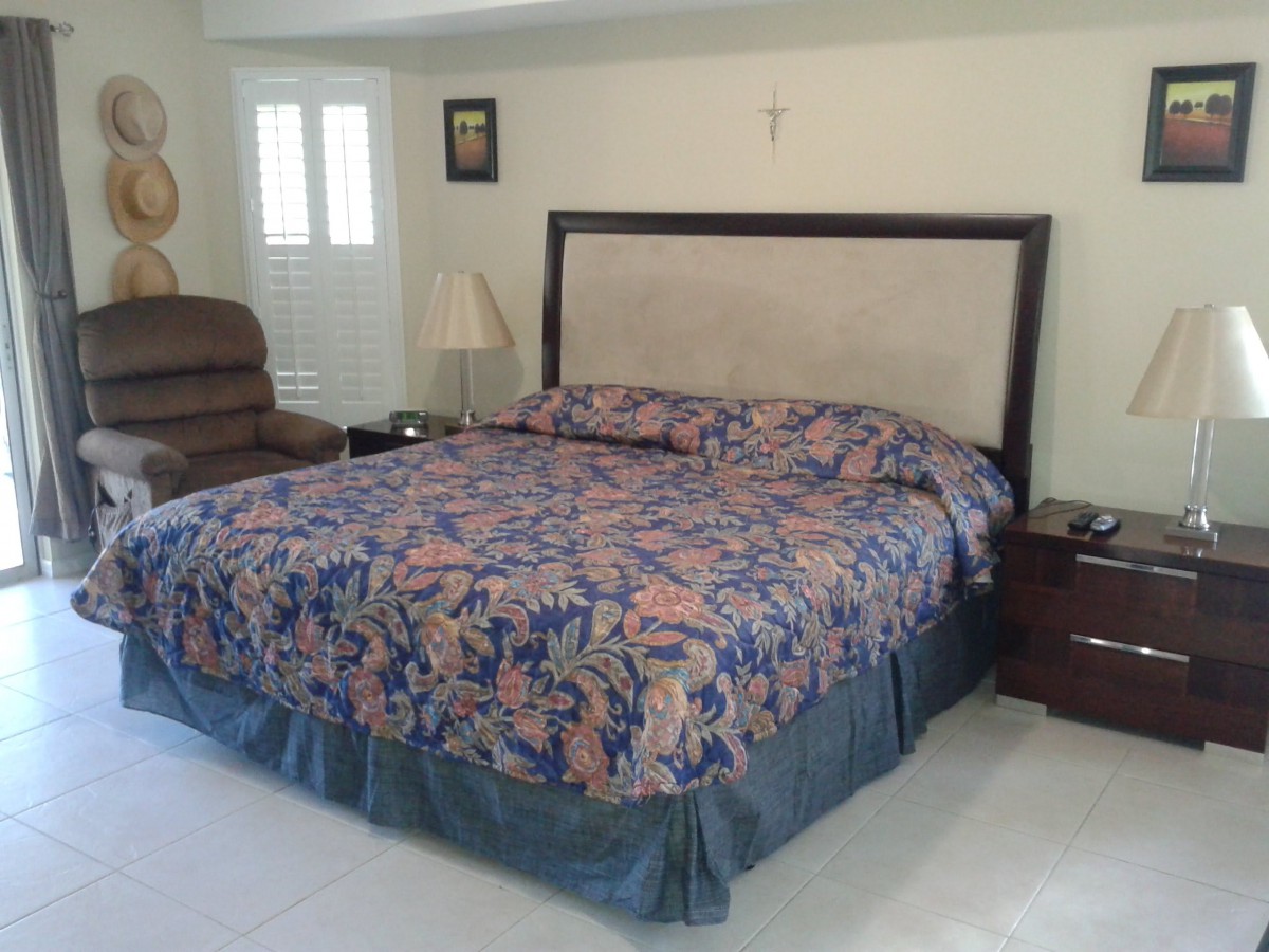 A cozy bedroom featuring a large bed with a floral comforter, a nightstand with a lamp, and an armchair in the corner.