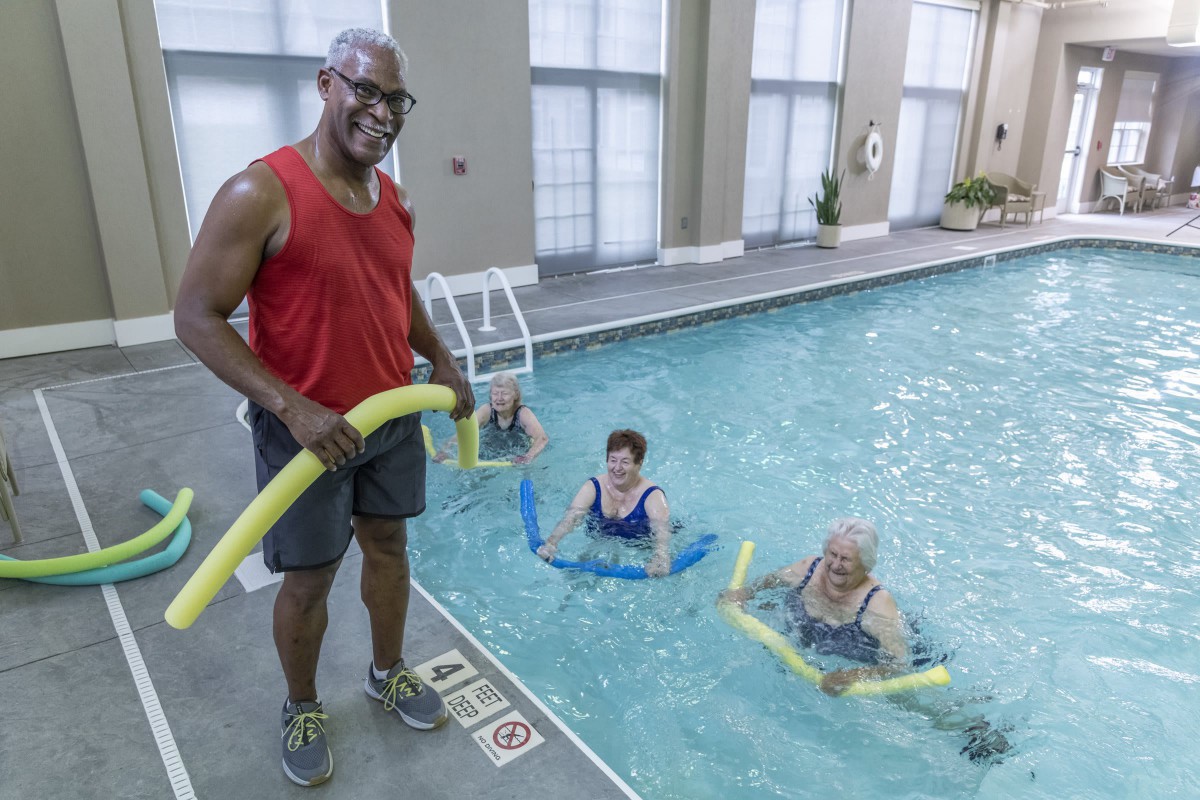 A group of seniors participating in an aquatic fitness class using pool noodles.