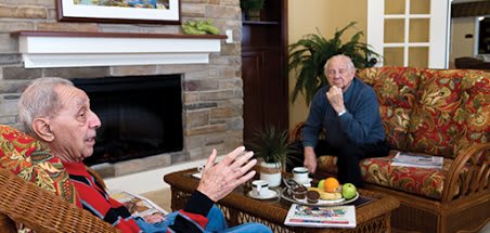 Two seniors having a conversation in a cozy living room setting with a coffee table between them.