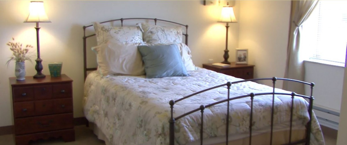 A cozy bedroom with a neatly made bed and a side lamp on the nightstand.