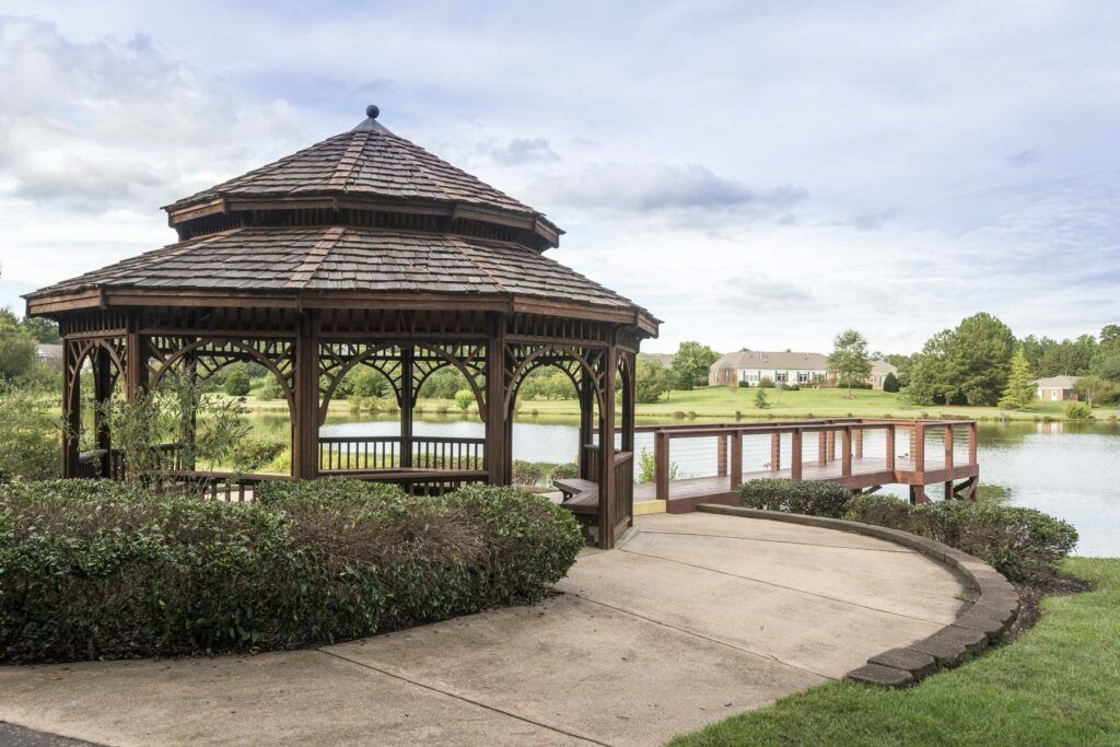 A scenic view of a gazebo by the lake with a pathway and lush greenery.