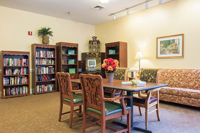 A cozy library room featuring a table with chairs, surrounded by bookshelves and decorative items.