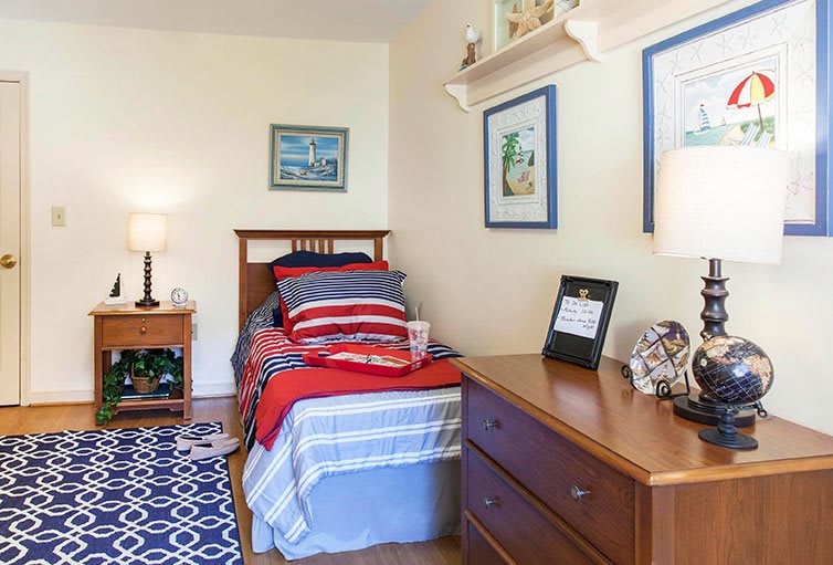 A cozy bedroom with a neatly made bed, wooden dresser, and decorative artwork on the walls.