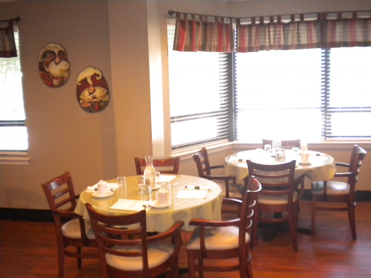A cozy dining area with round tables, wooden chairs, and natural light streaming through the window.