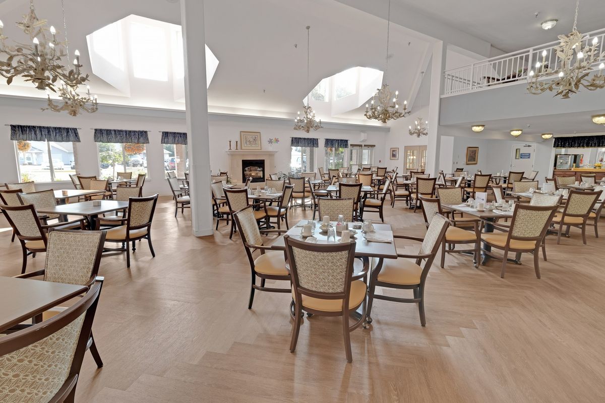 A spacious and bright dining room with elegantly set tables and chairs under decorative chandeliers.