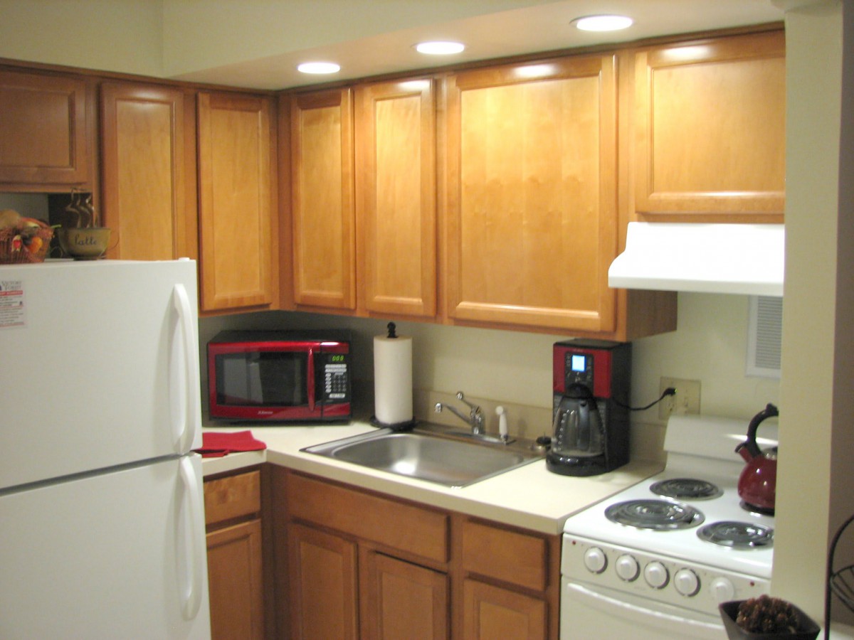 A compact, modern kitchen with wooden cabinets and various appliances including a refrigerator, microwave, coffee maker, stove, and sink.