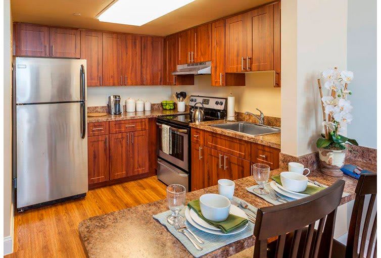 A modern kitchen with wood cabinets, stainless steel appliances, and a neatly set dining table.