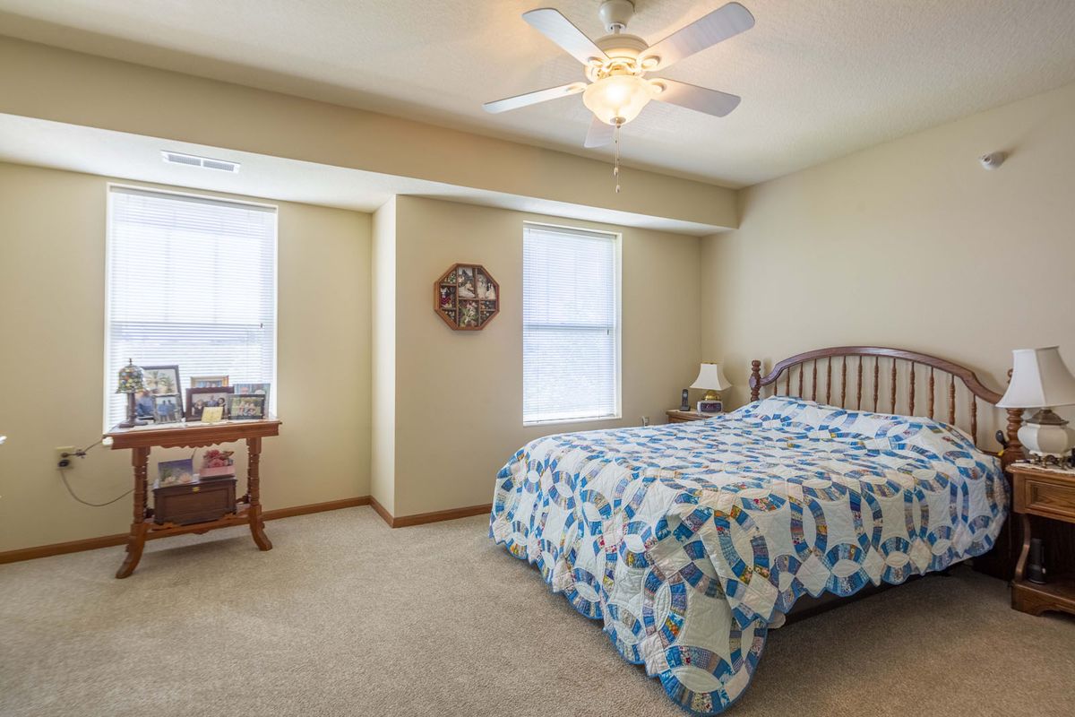 A cozy bedroom with a bed, ceiling fan, and natural light from windows.