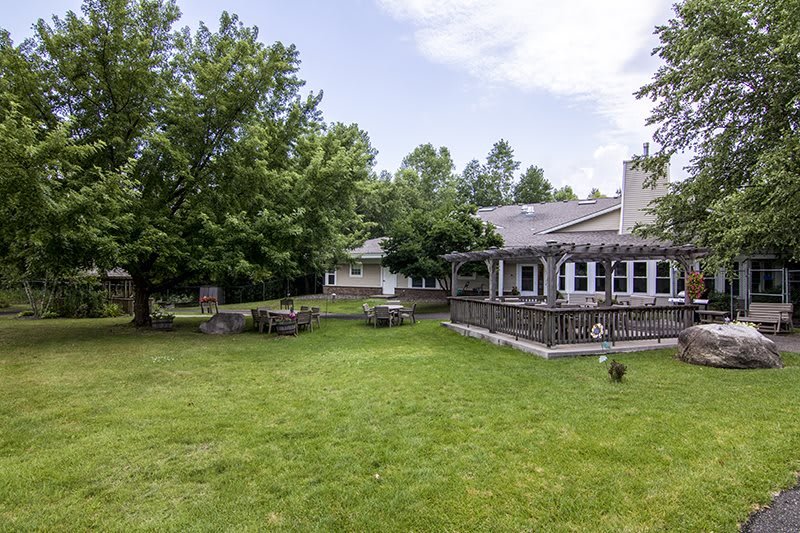 A serene backyard with a spacious lawn, surrounded by trees and featuring a house with a porch.