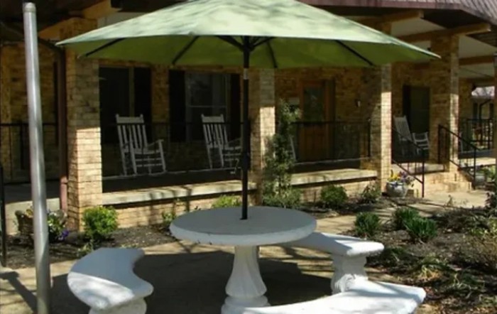 A cozy outdoor patio area with a round table and umbrella, surrounded by benches and rocking chairs.