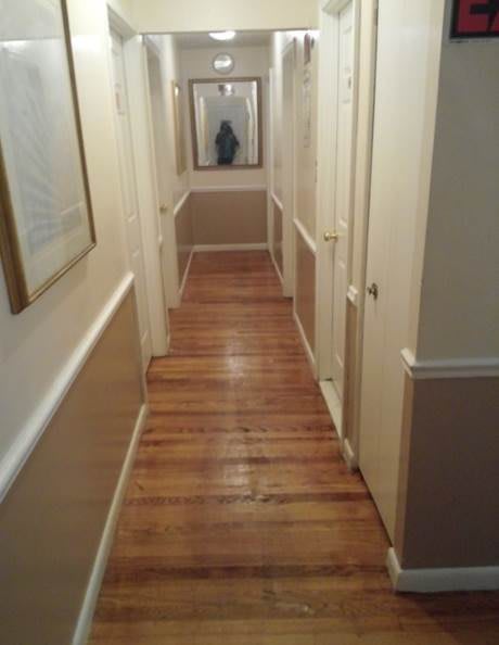 A narrow hallway with a wooden floor and a mirror at the end.