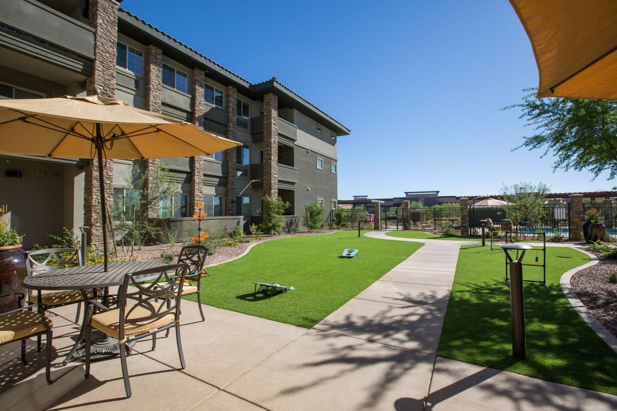 A modern apartment complex with a landscaped outdoor area featuring a synthetic lawn and patio furniture under sunny skies.