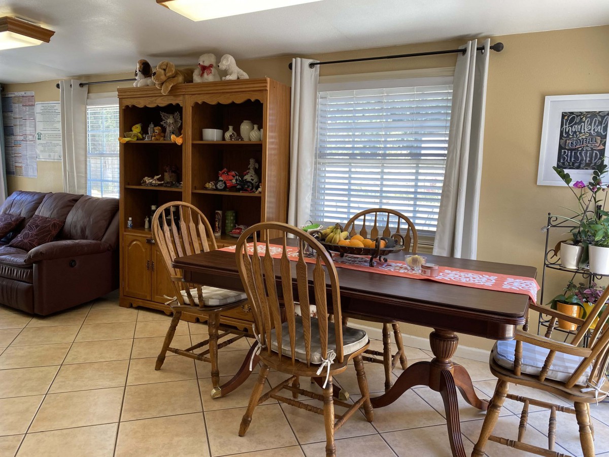 A cozy dining room featuring a wooden table with chairs, and a shelf filled with various decorative items.