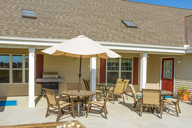 A cozy patio setup with chairs, a table, and an umbrella beside a barbecue grill.