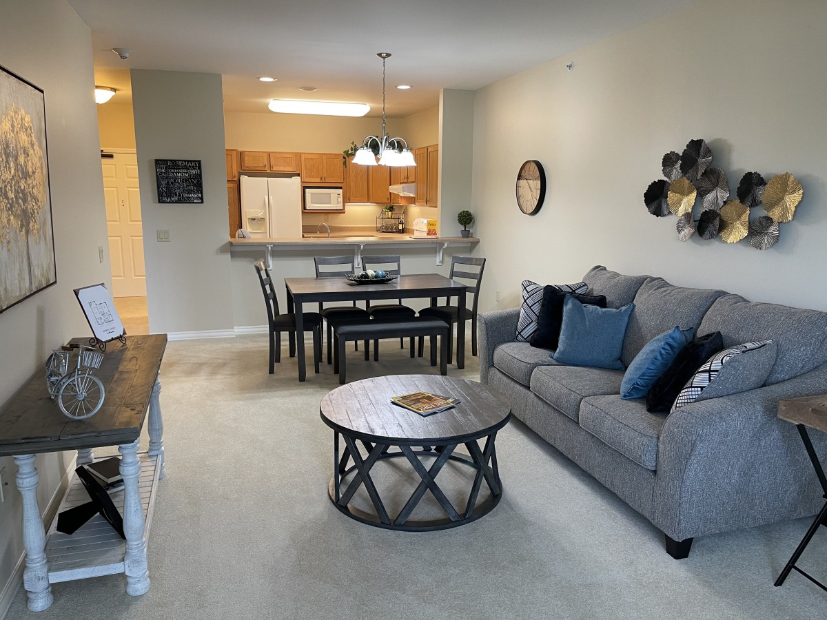 A cozy open-plan living room with a kitchen and dining area, furnished with a comfortable sofa, coffee table, and dining set.