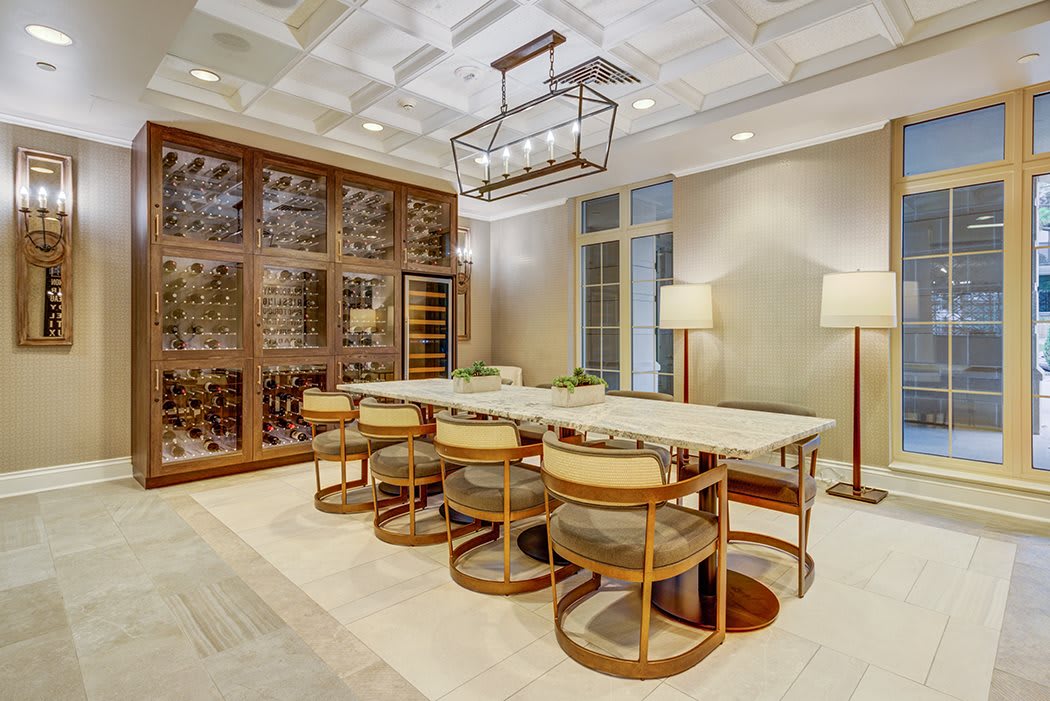 A modern dining room with a large table, stylish chairs, and an elegant chandelier, featuring a wall-mounted wine rack.
