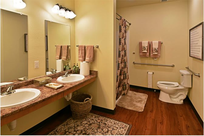 A warmly decorated bathroom with dual sinks, a shower curtain, and wooden flooring.