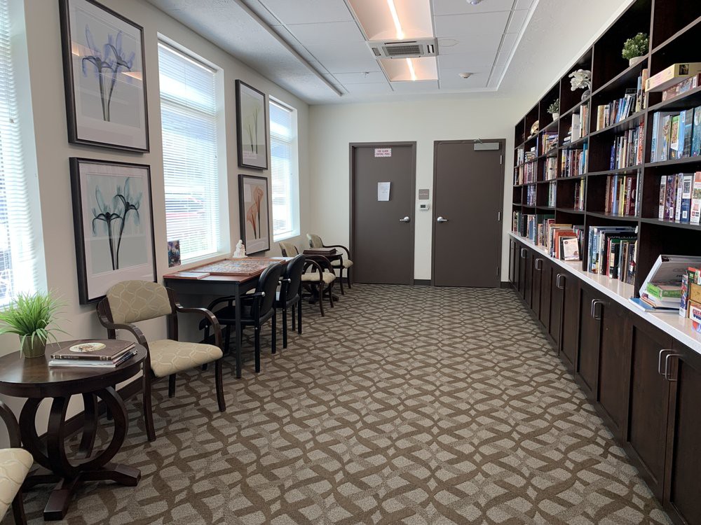 A quiet waiting room with chairs, a bookshelf, and artwork on the walls.
