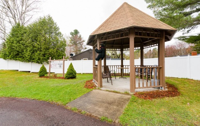 A wooden gazebo in a garden setting with a surrounding fence and lush greenery.