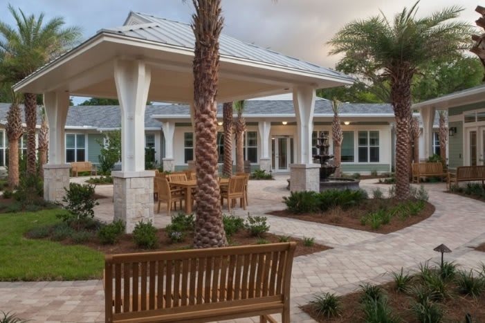 A serene outdoor patio area with benches and palm trees in front of a modern building.
