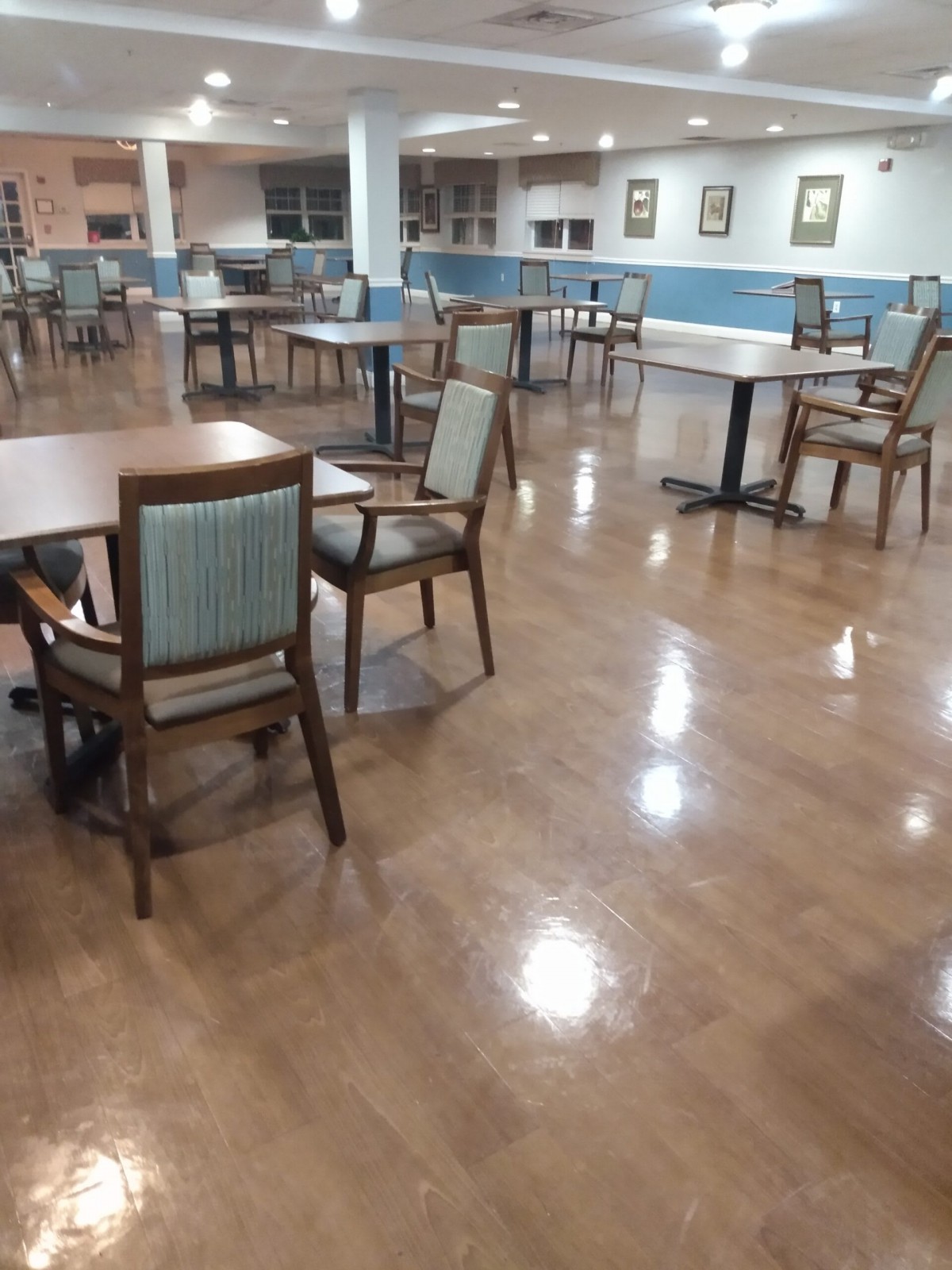 An empty dining area with wooden tables and chairs on a polished floor.
