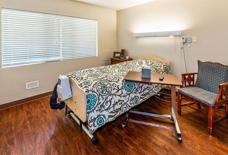 A hospital room featuring a single bed with a patterned bedspread, equipped with medical necessities.