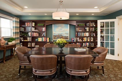 A cozy library meeting room with bookshelves and a central table surrounded by chairs.