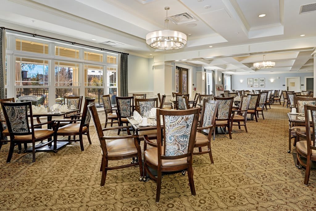 An elegant dining room with neatly arranged tables and chairs under a chandelier.