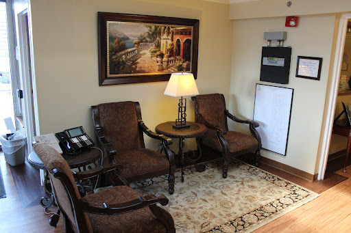 A cozy living area featuring brown upholstered chairs, a lamp on a side table, and a scenic artwork on the wall.