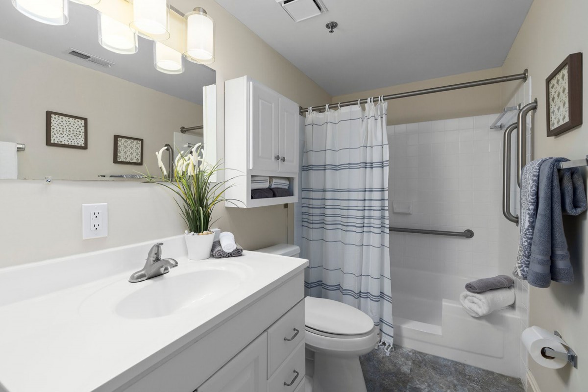 A modern bathroom with a sink, toilet, and shower area, featuring a plaid shower curtain and overhead lighting.