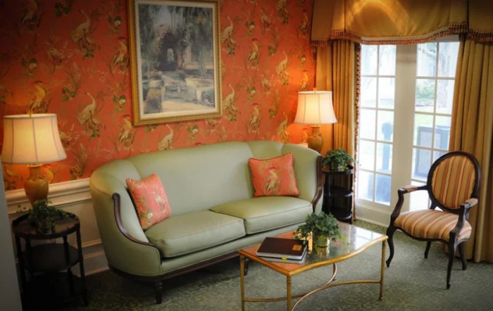 A cozy living room with a pastel green sofa, accompanied by matching decorative pillows and a classic lamp next to a patterned wall.