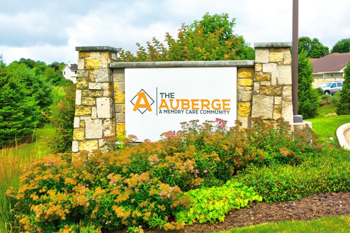 A stone sign for 'The Auberge Community' surrounded by lush greenery.