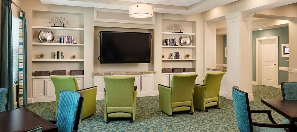 A modern living room with green chairs facing a large television and built-in shelves.