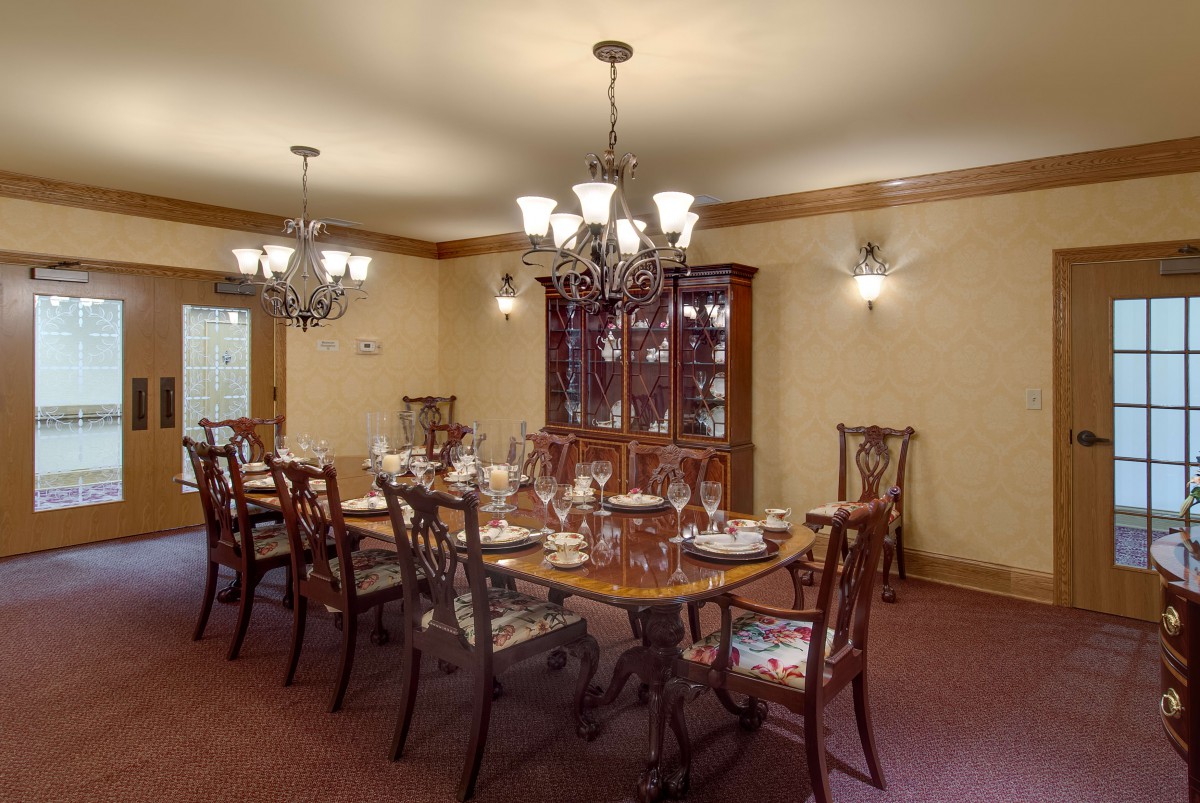 An elegant dining room with a large wooden table, surrounded by chairs and illuminated by chandeliers.