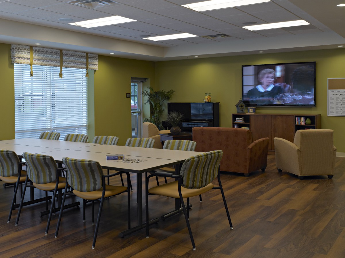 A modern meeting room with a large conference table, comfortable lounge chairs, and a television.