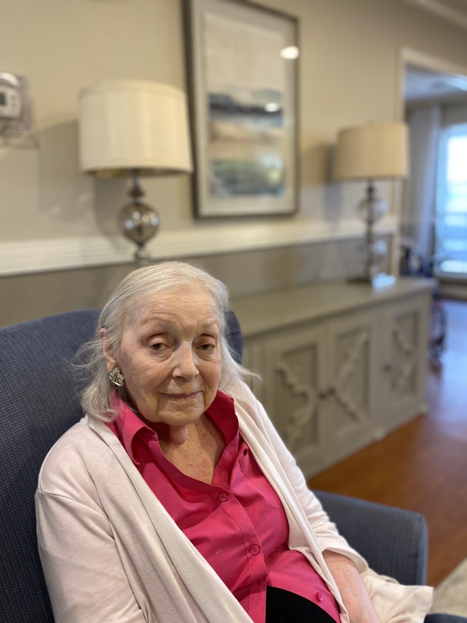 An elderly woman sitting in a chair in a cozy living room setting.