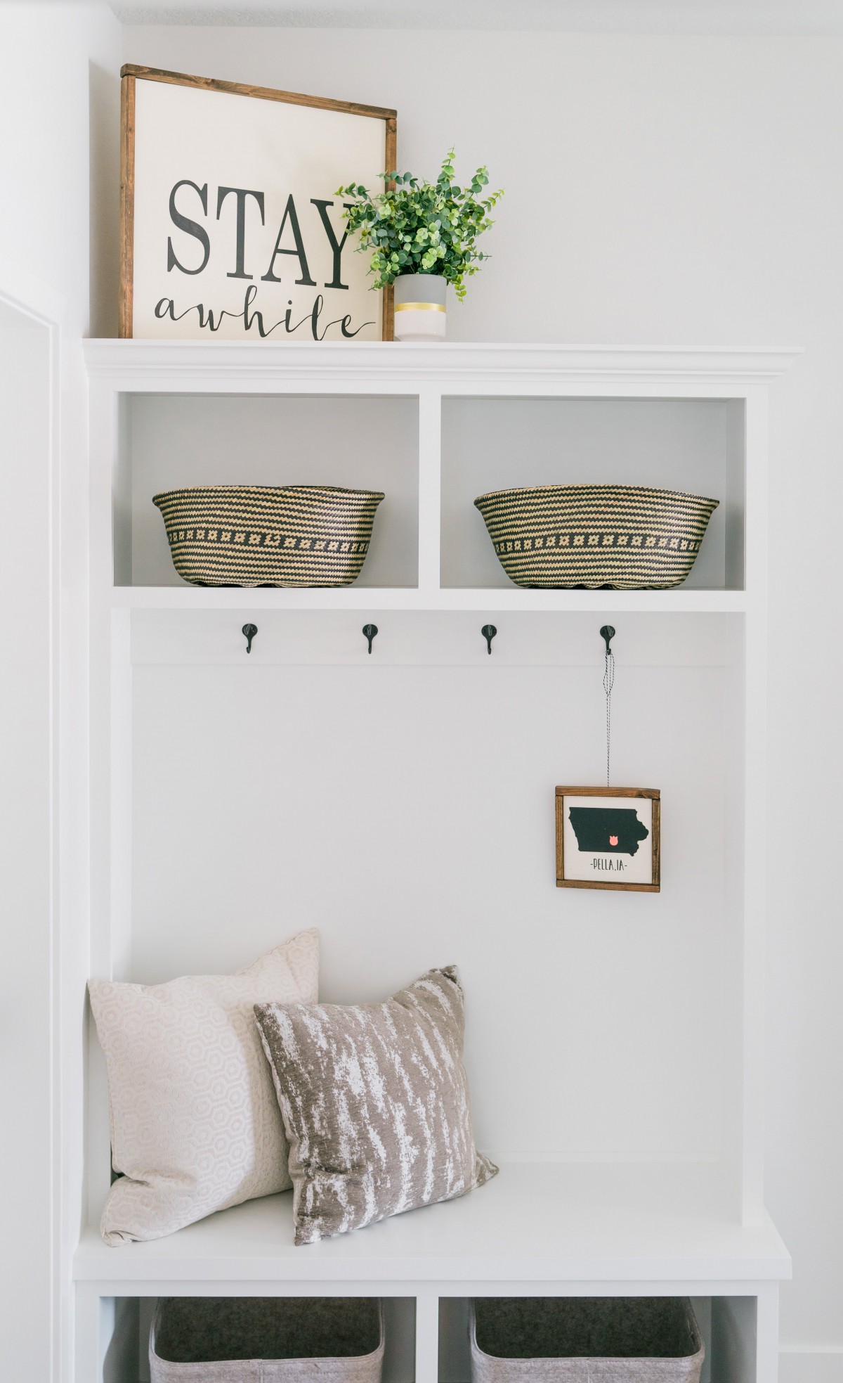 A neatly organized entryway with baskets for storage, hooks for hanging items, and a cushion for seating, showcasing minimalist home decor.