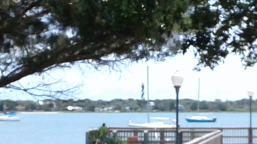 A serene waterfront view featuring trees, a dock, and sailboats in the distance.