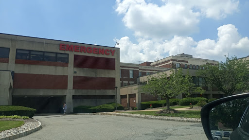 A view of a hospital building featuring the emergency room entrance, set against a partly cloudy sky.