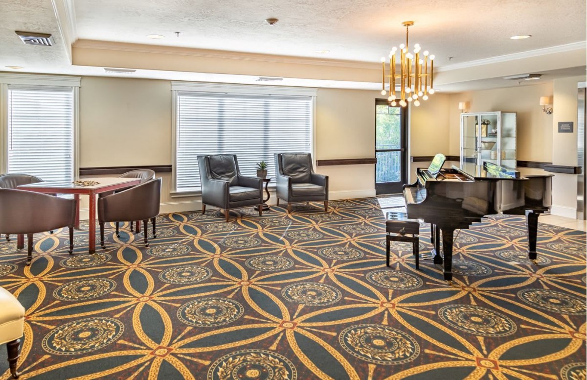 A spacious lounge area with elegant furnishings, featuring a piano and a modern chandelier.