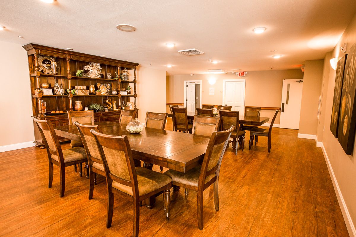 A spacious dining room with wooden tables and chairs, featuring a large bookshelf and warm lighting.