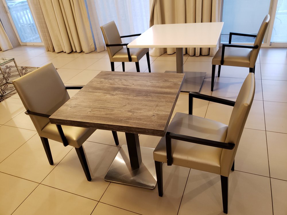 A dining area with square tables and cushioned chairs, arranged in a tiled room.