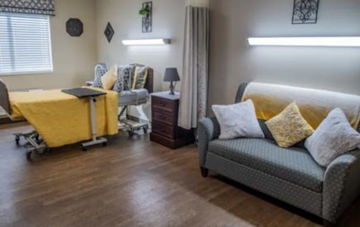 A cozy hospital room with a bed, sofa, and bedside table.